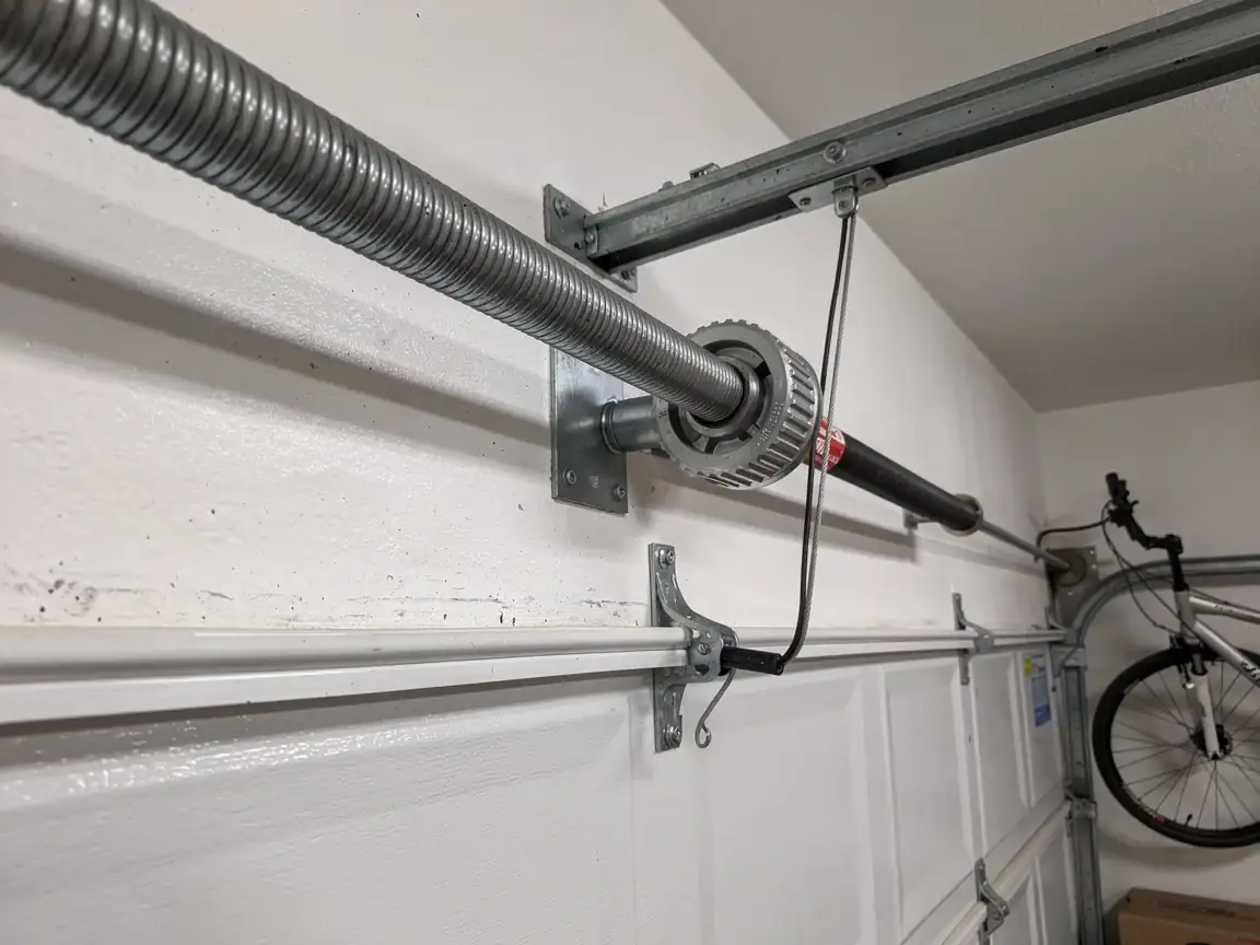 A garage door torsion spring is mounted above a white garage door.